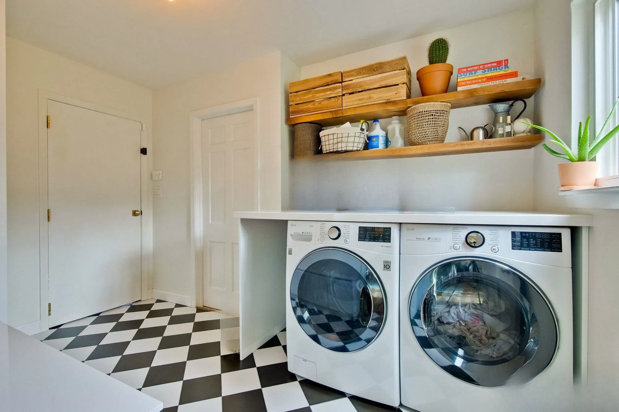 Laundry with a stacked washer and dryer, timber shelving and a checkerboard tile floor