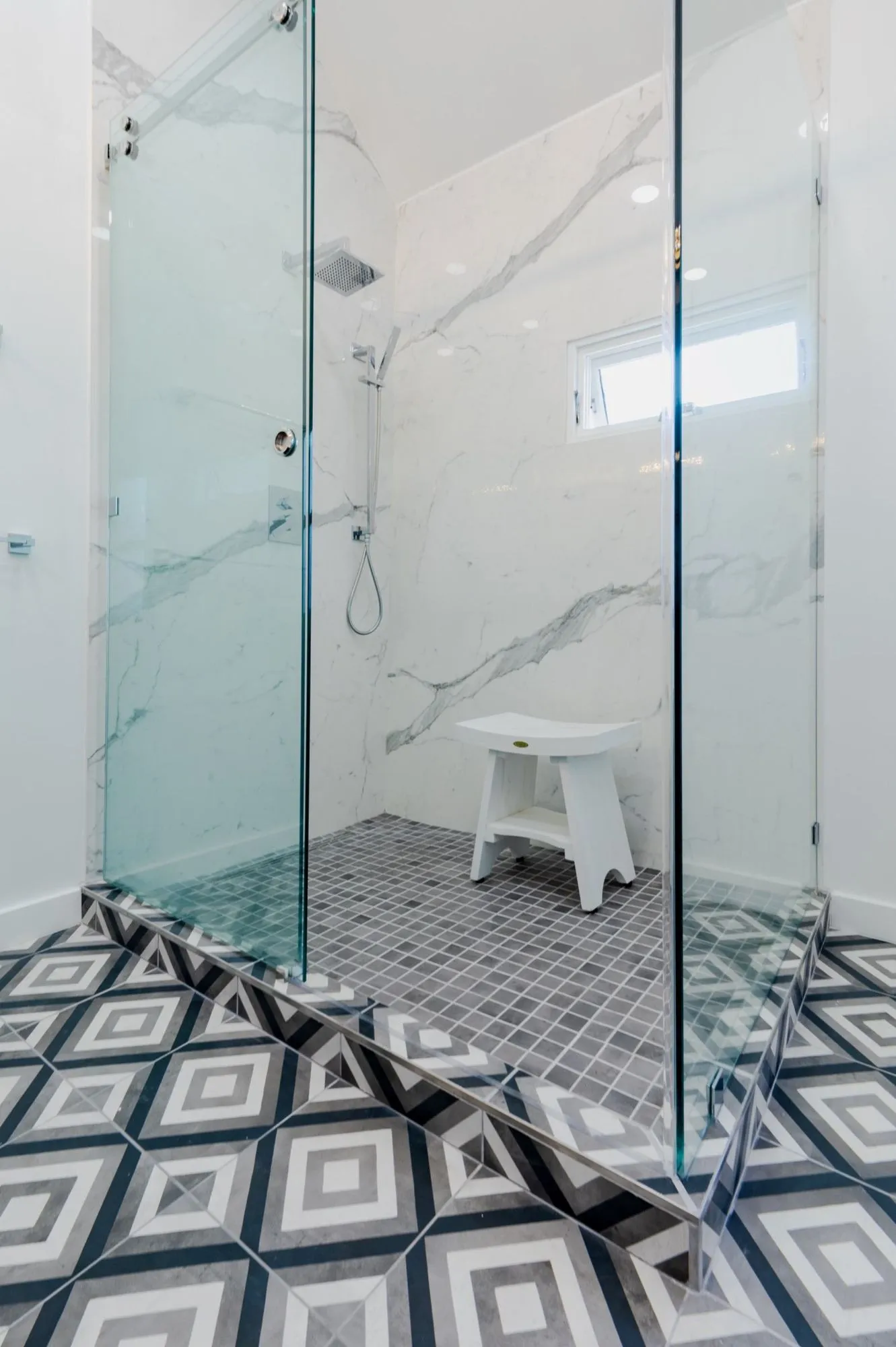 Marble-veined slab shower after remodel above geometric patterned floor tile