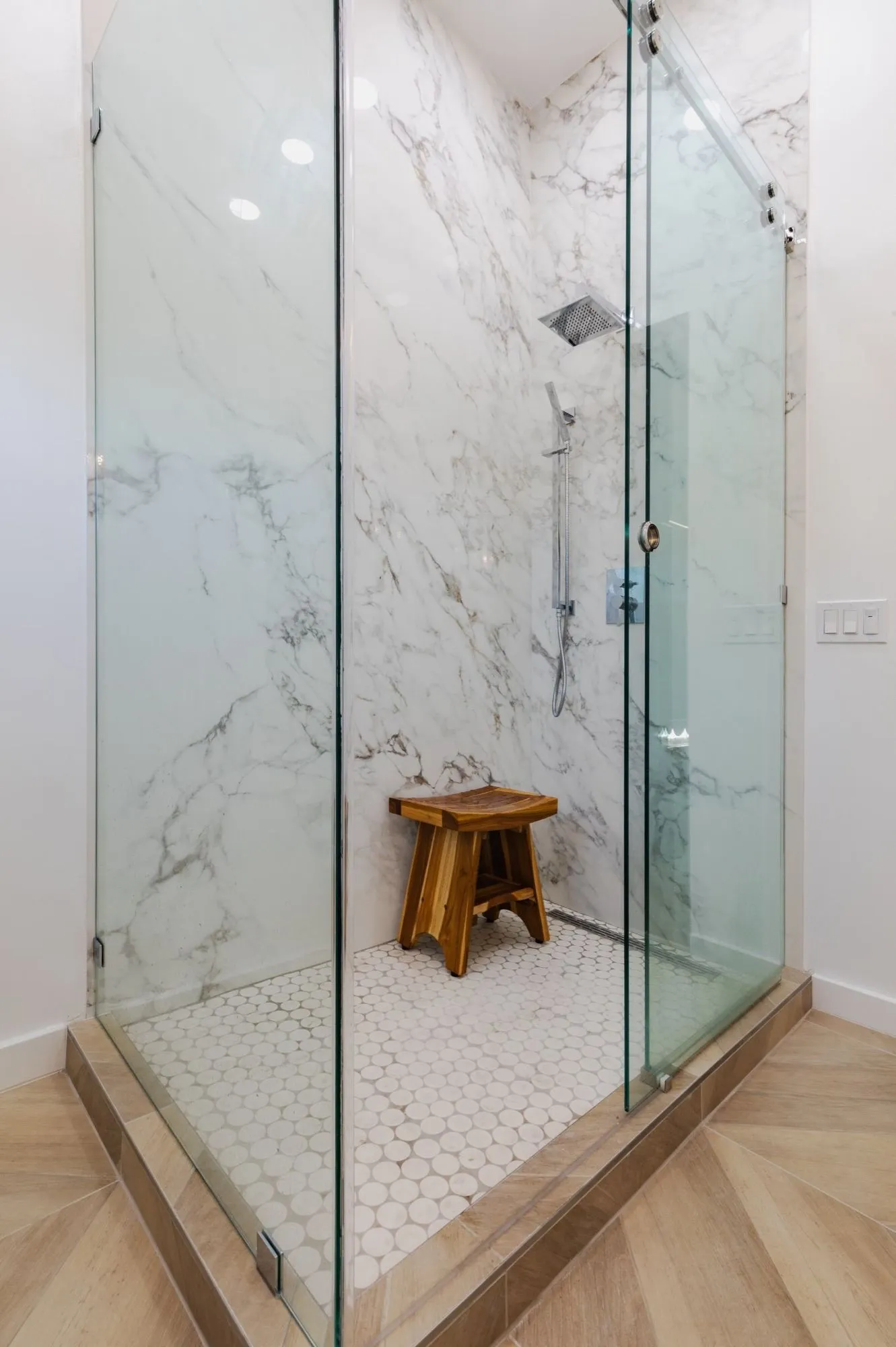 Marble-veined slab shower with teak stool and white hex tile floor
