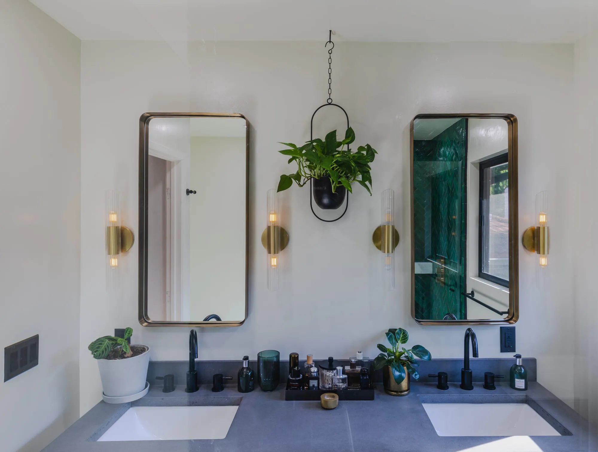 The pair of brass-framed mirrors with a hanging plant between them above twin basins