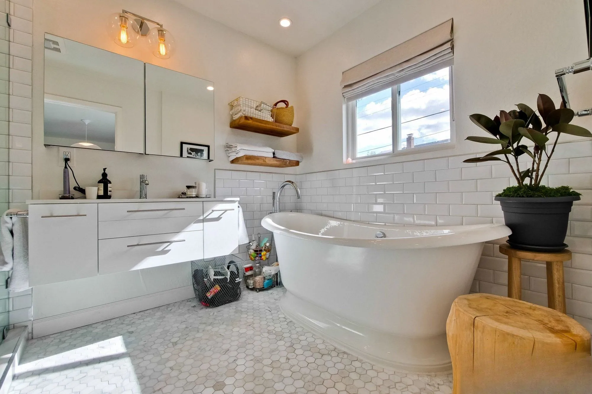 Freestanding tub against white subway tile with a timber shelf and potted plant
