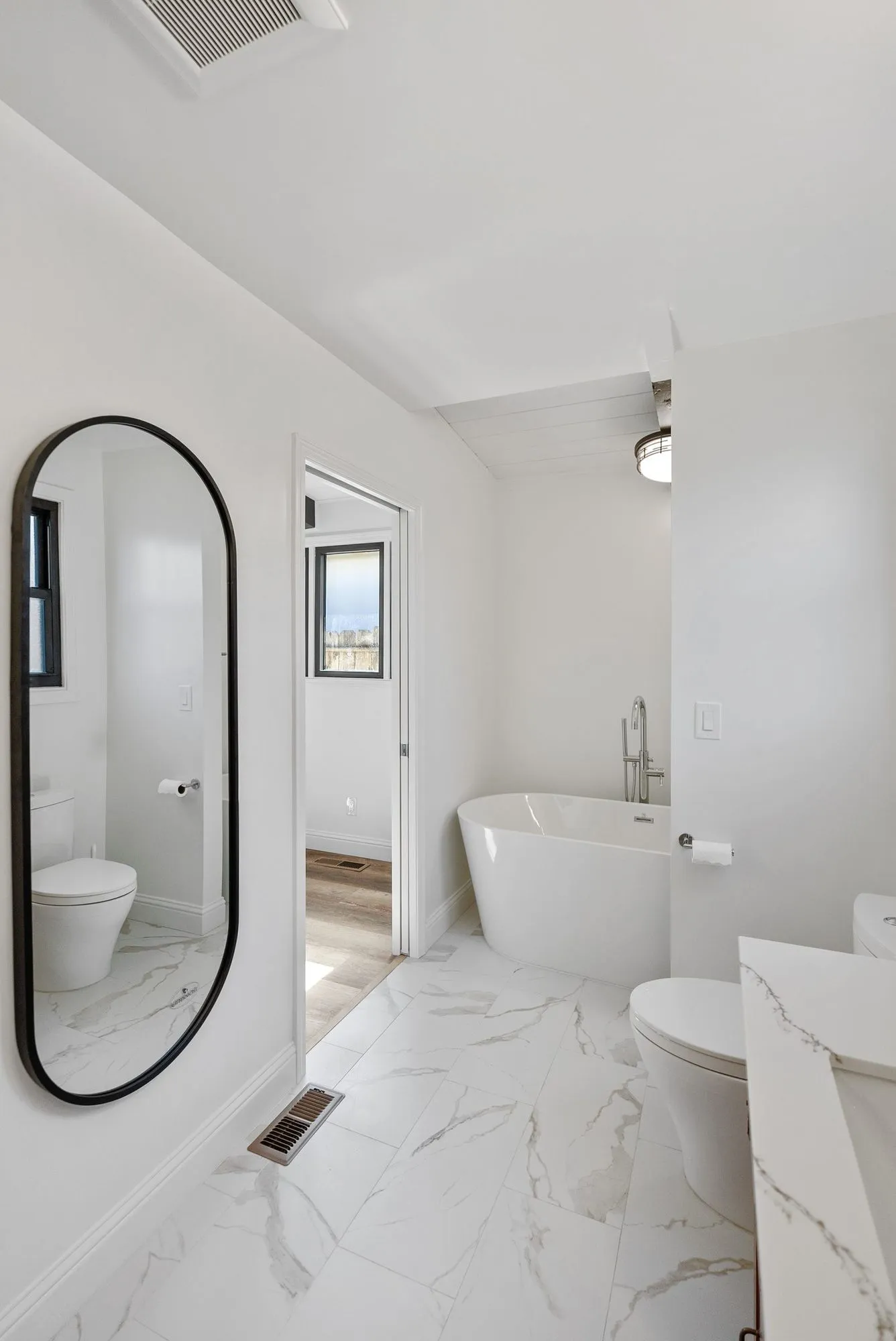 Bathroom finished in marble-look tile with a freestanding tub and a tall arched mirror