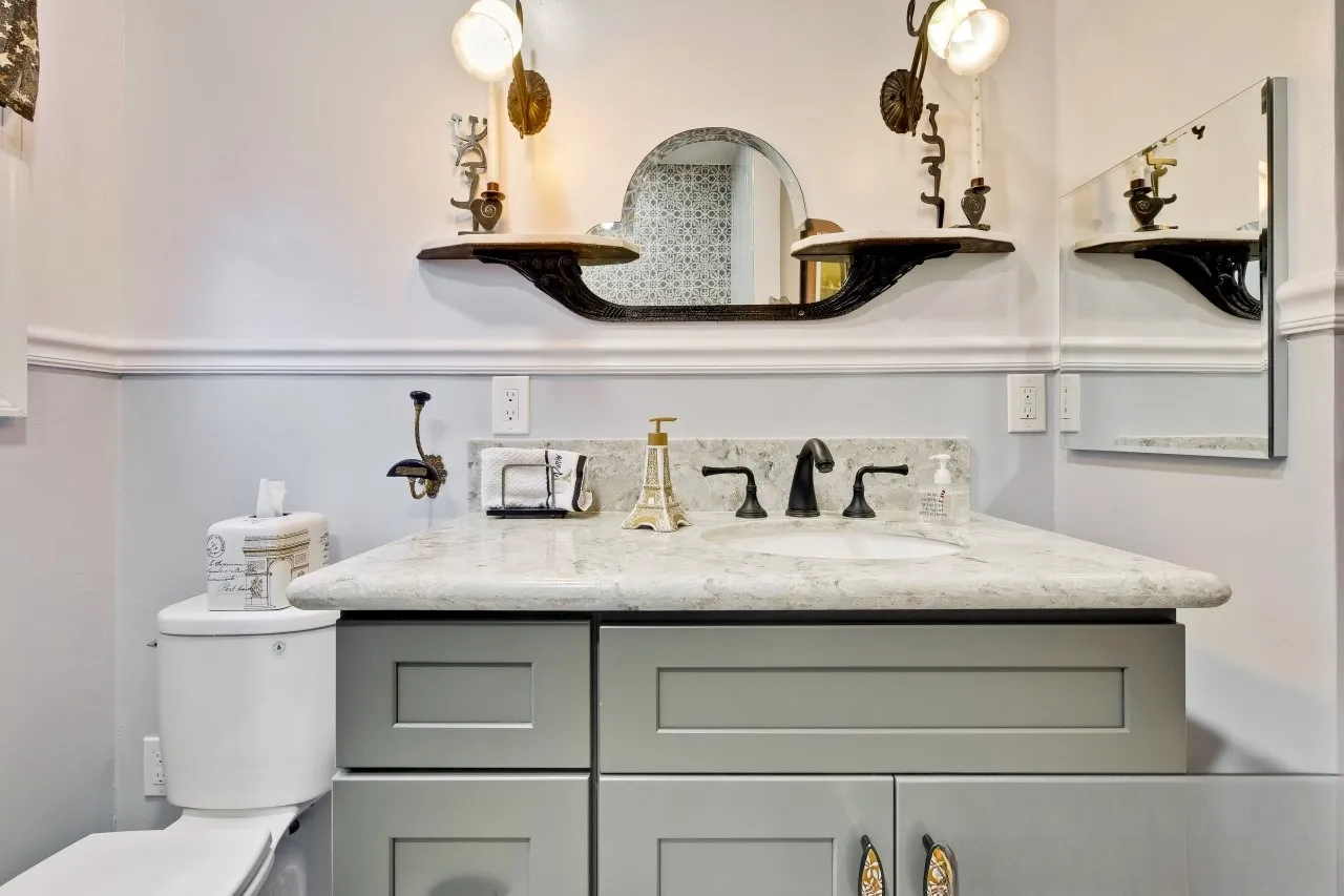 Sage shaker vanity with a veined stone counter, oil-rubbed bronze tapware and an arched mirror above