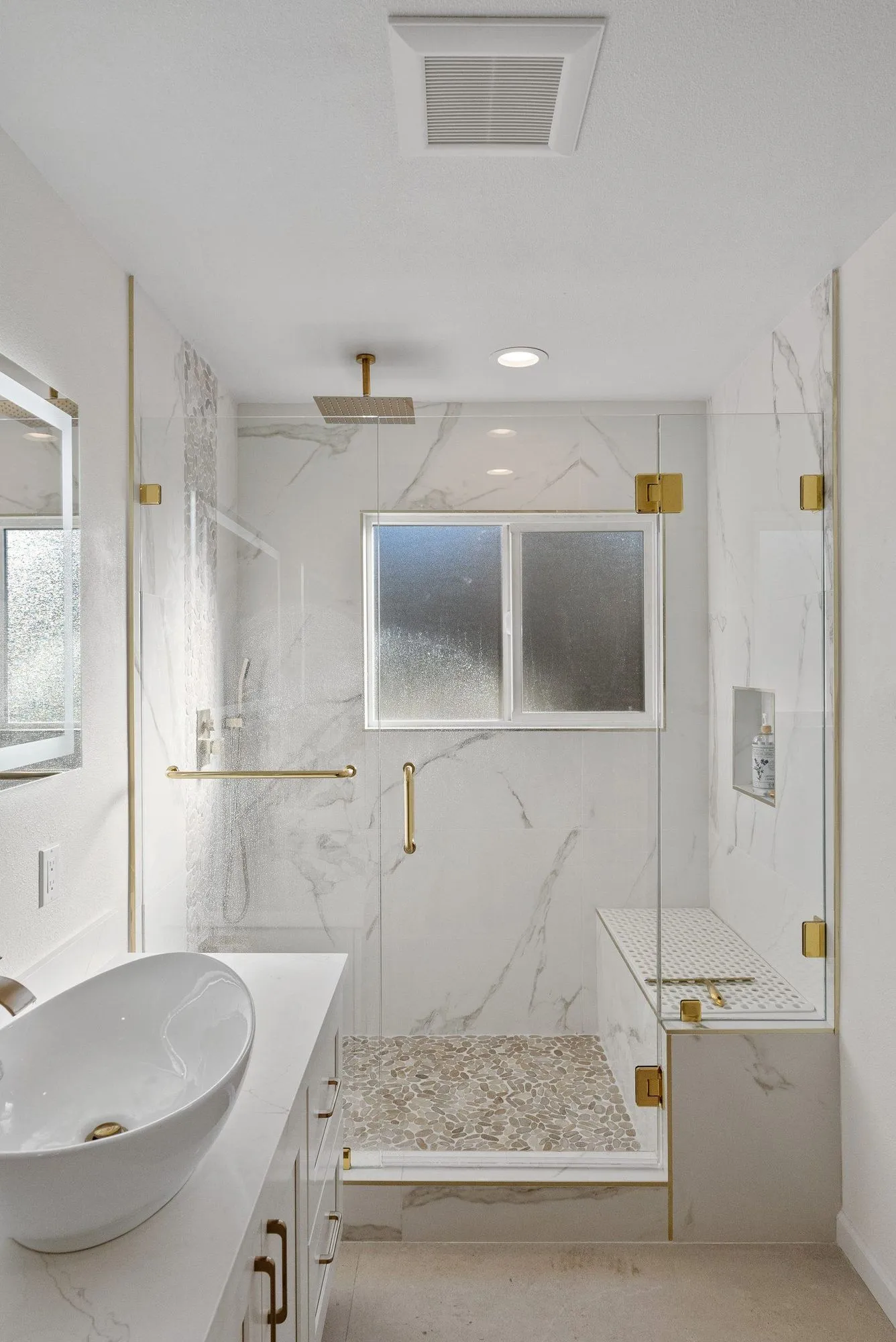 Shower and vanity finished in large-format marble-look slab with brass fittings