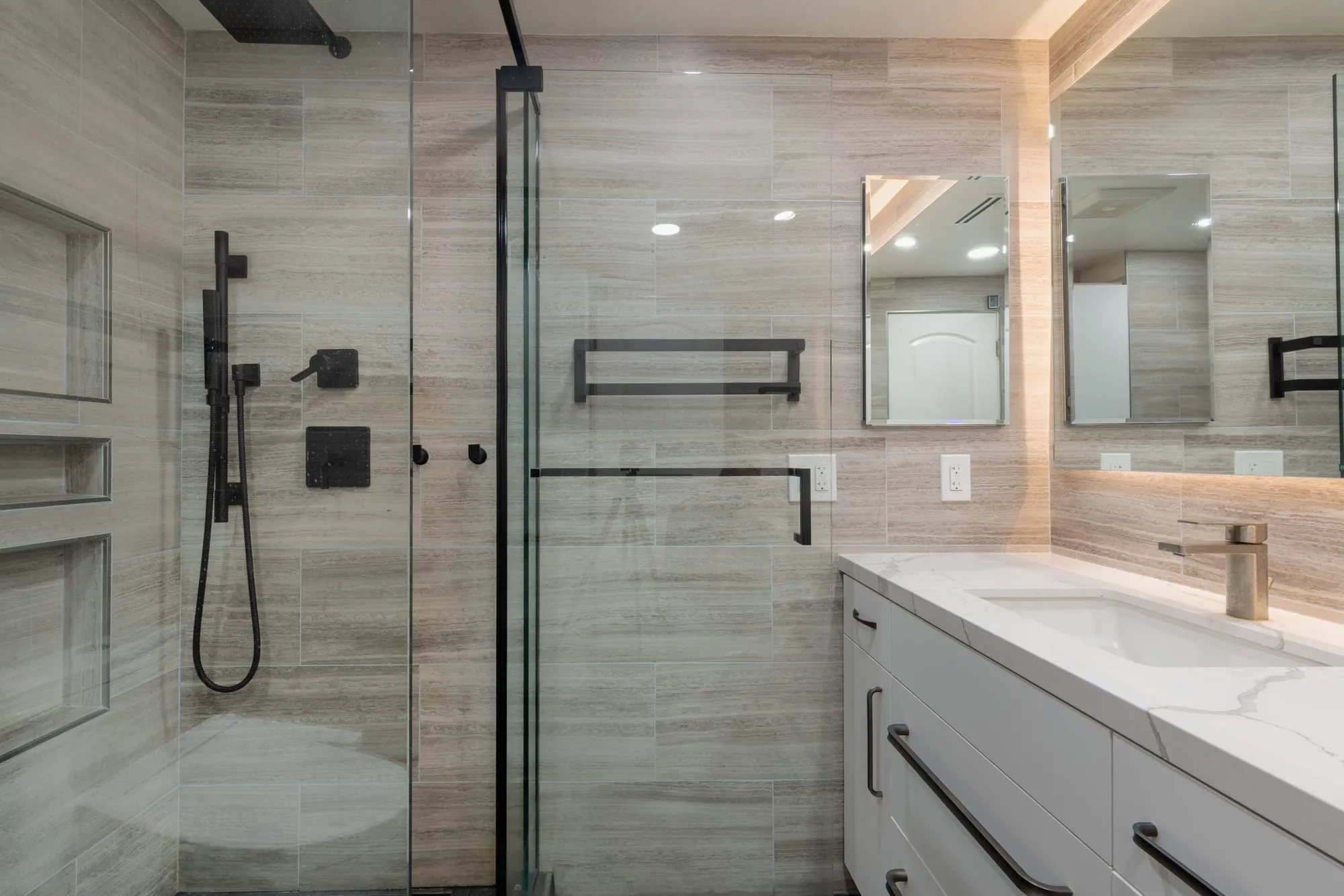 View across the room from the shower glass to the vanity and backlit mirror