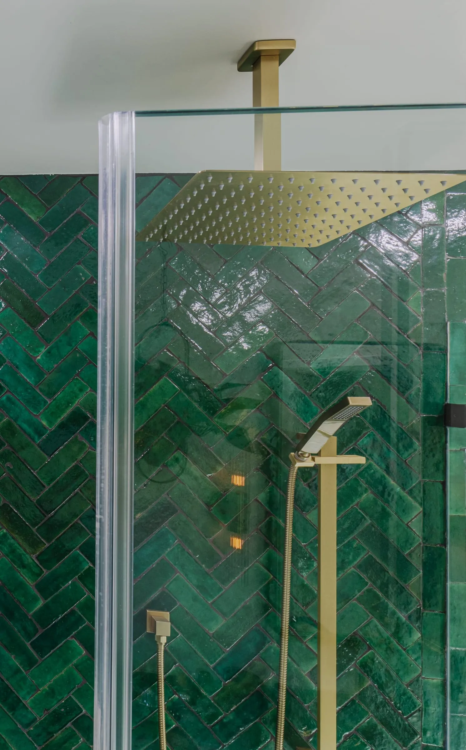 Frameless glass panel to the shower with the brass shower set against the emerald tile
