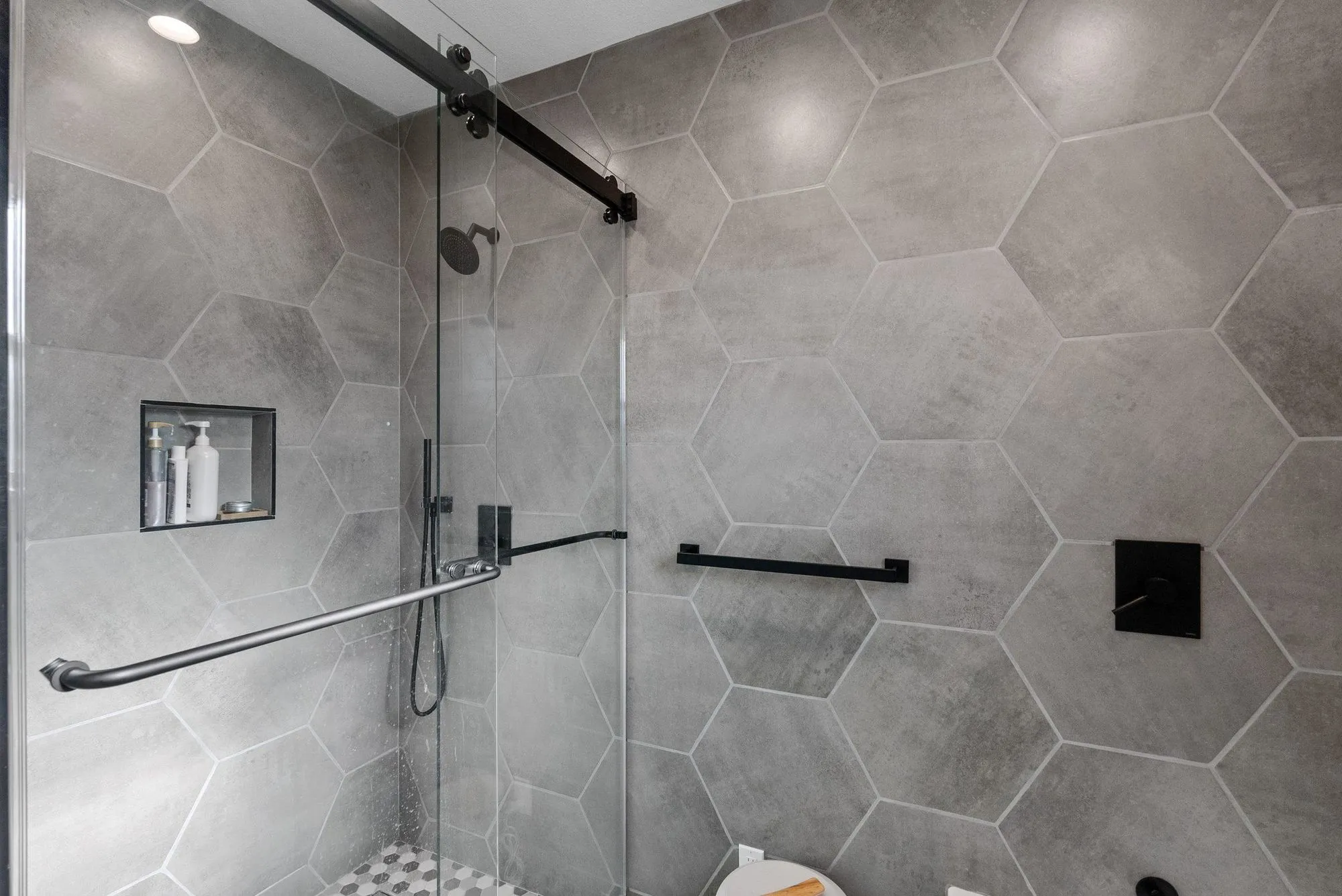 Shower enclosed in glass with grey hexagonal tile and a recessed niche