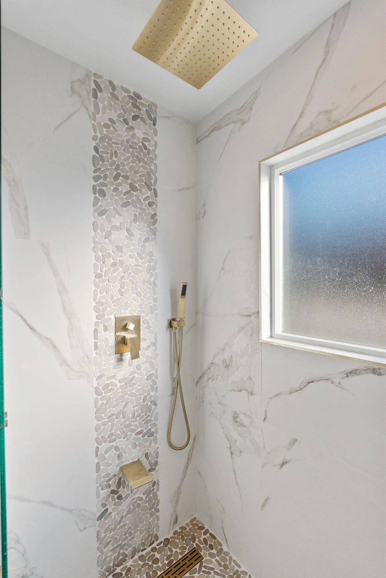 Walk-in shower in marble-look slab with a brass rain head and a mosaic feature strip