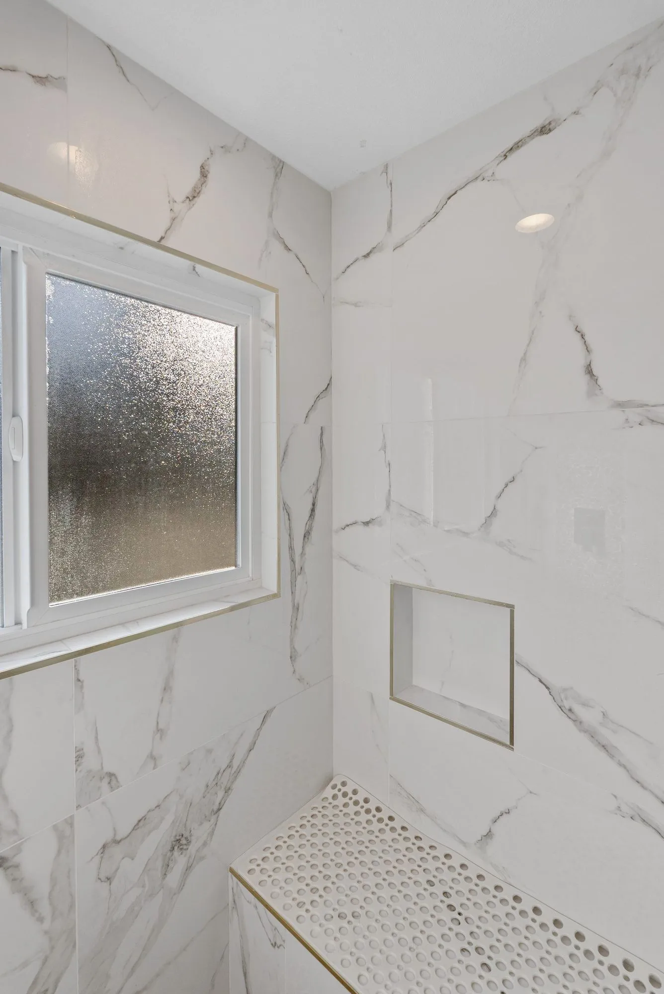 Shower in marble-look slab with a frosted window and a mosaic-tiled bench