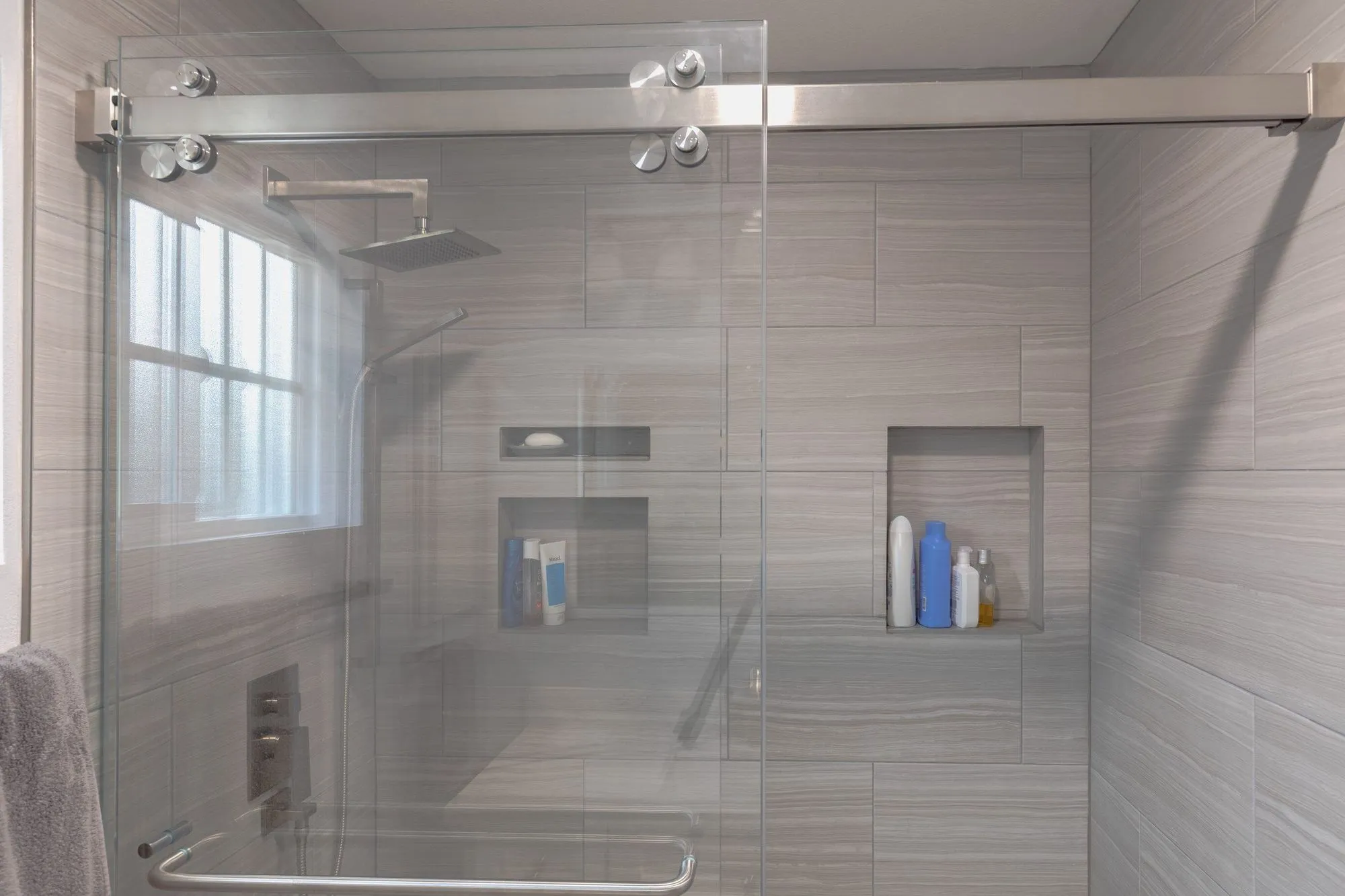 Wide walk-in shower behind full-height glass with twin recessed niches