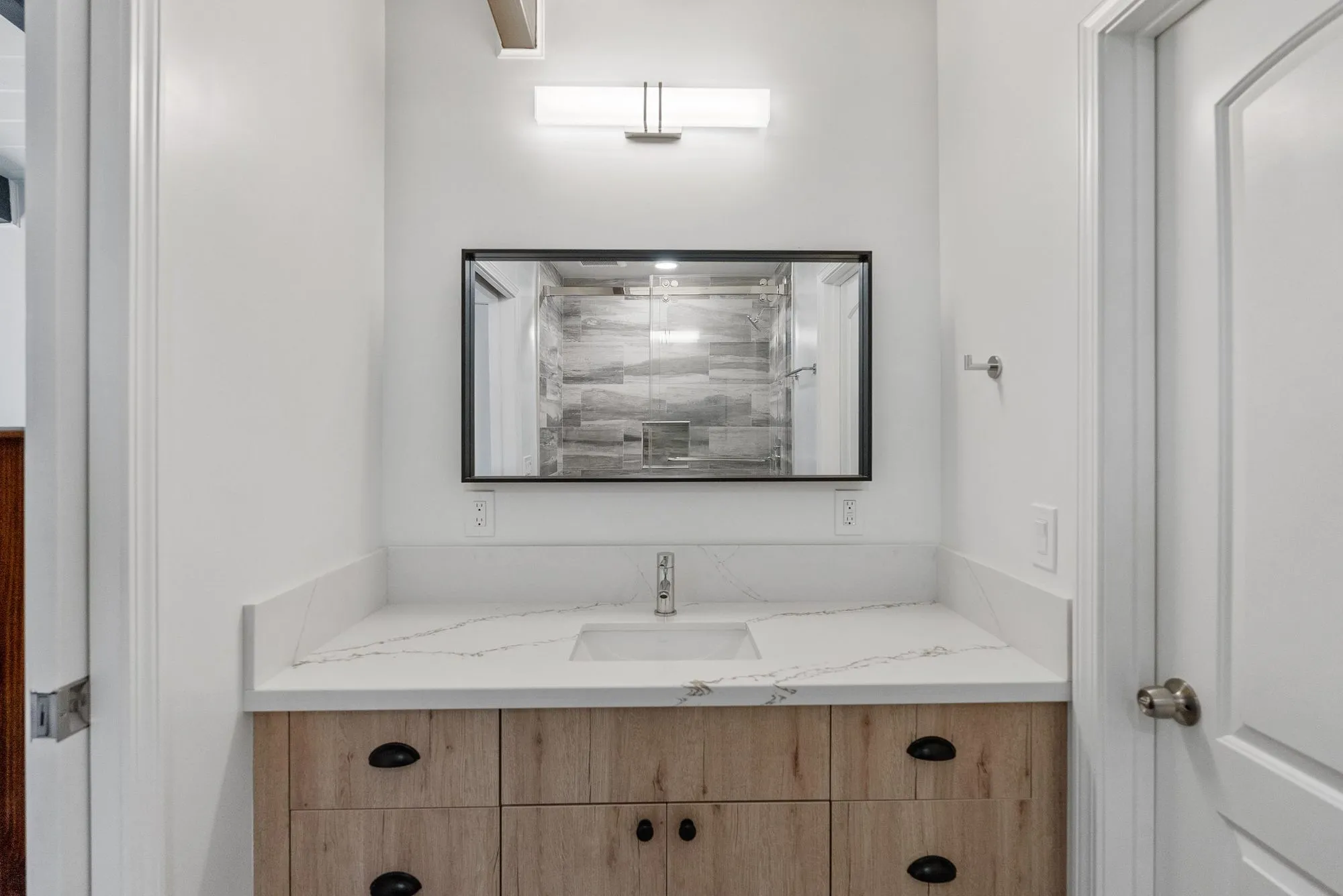 Single vanity in light oak with a quartz top, black hardware and a black-framed mirror
