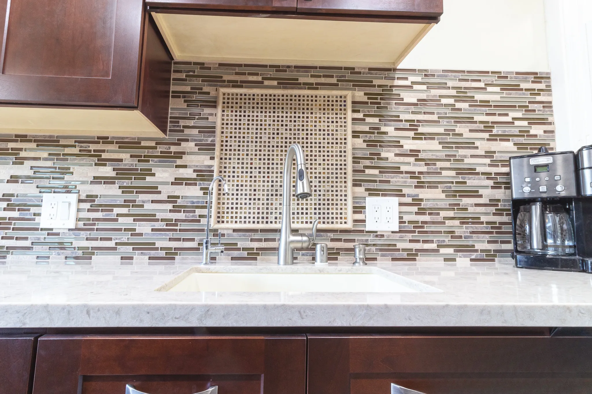 Undermount sink with pull-down tap against the glass mosaic backsplash and a square mosaic inset above