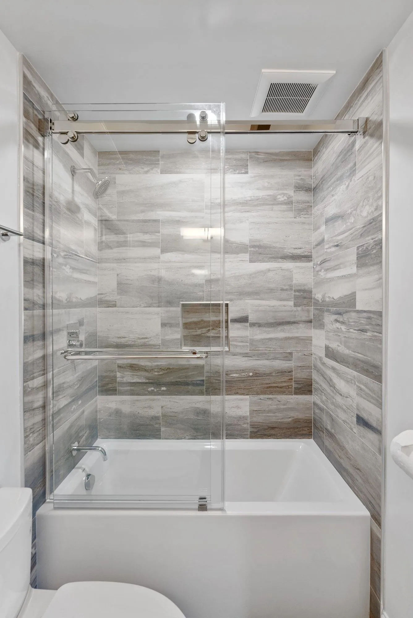 Tub and shower surround in stone-look plank tile behind a sliding glass panel