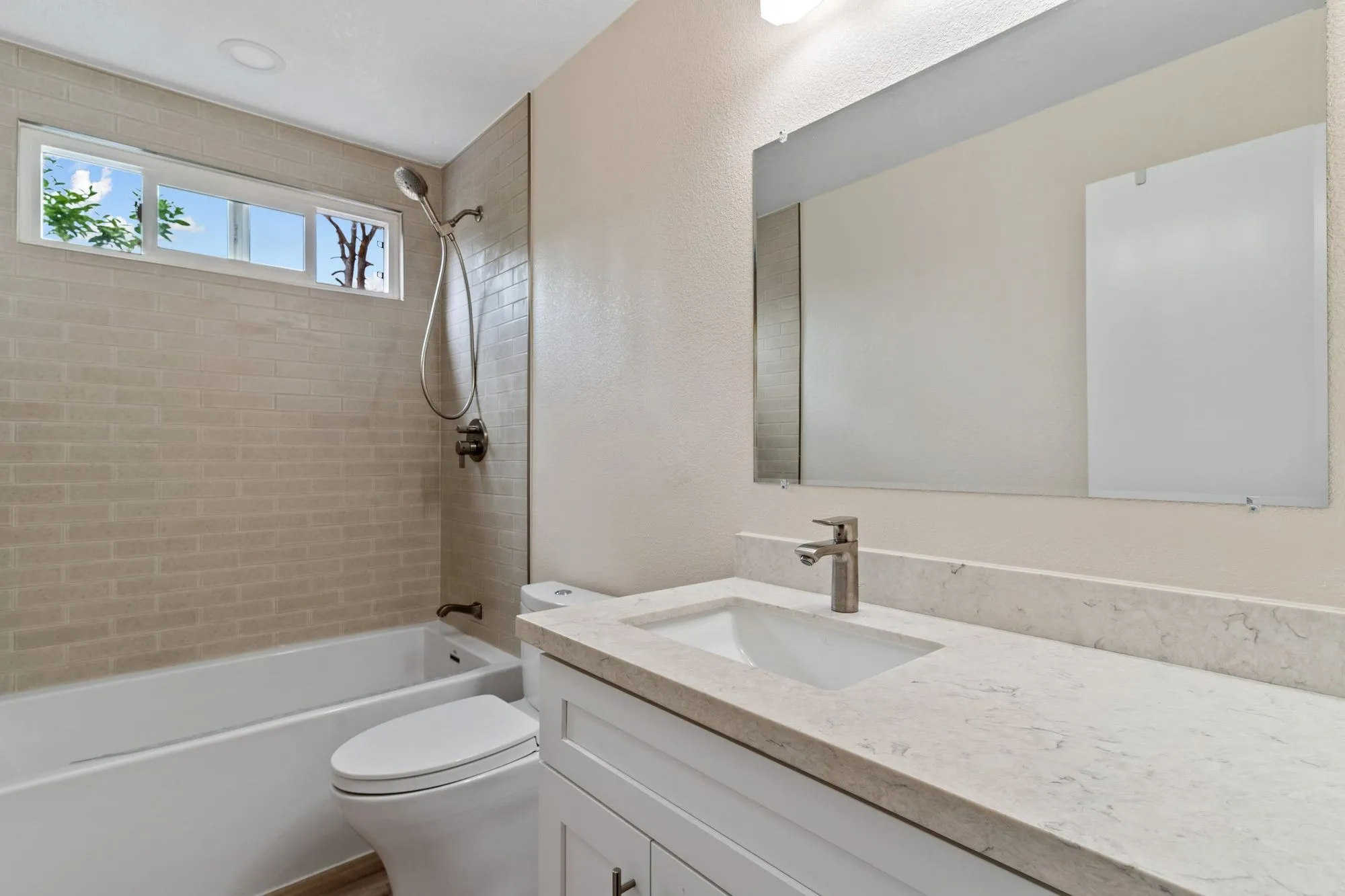Alcove tub and shower beside a vanity with a large frameless mirror