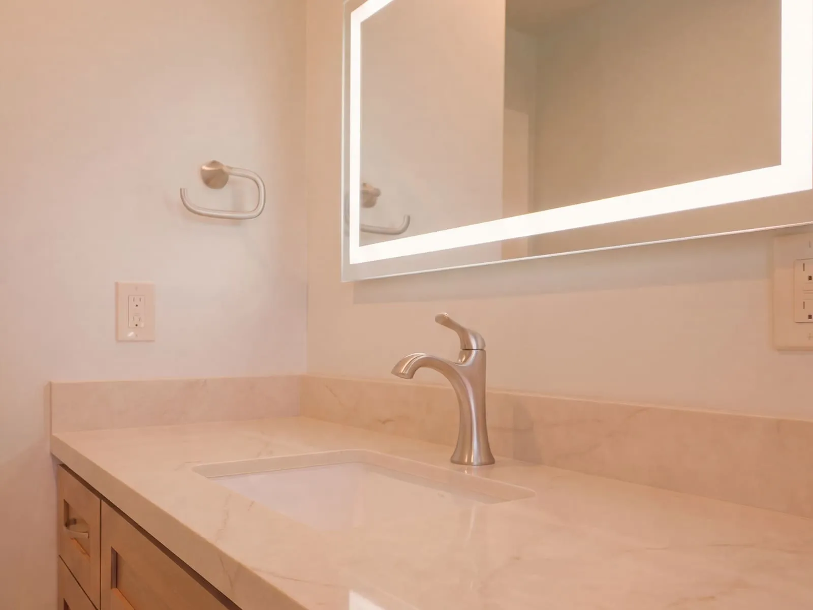 Wood vanity with a quartz top, undermount basin and a brushed-nickel tap below a lit mirror