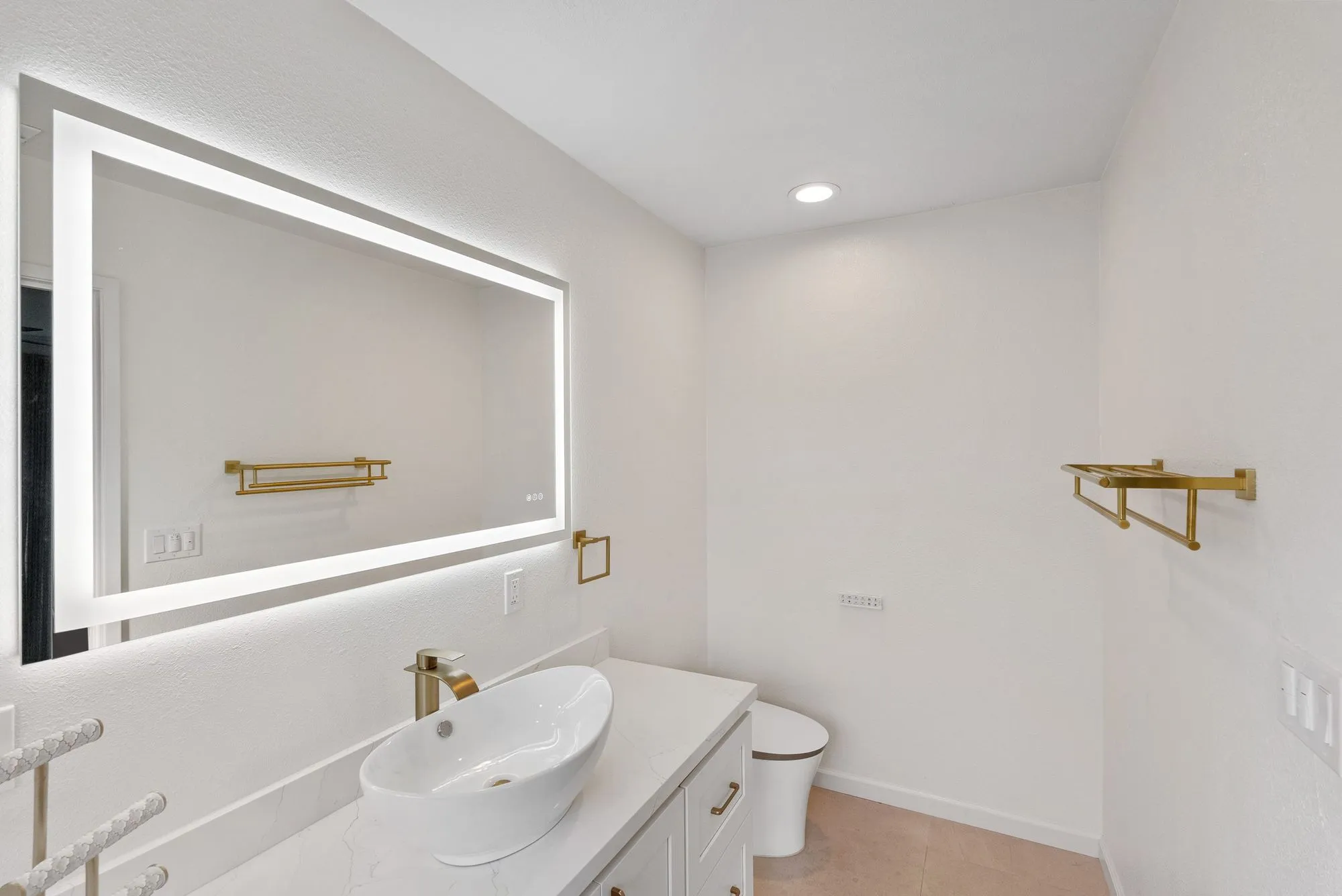 Vanity with a vessel basin below a backlit mirror and brass fittings