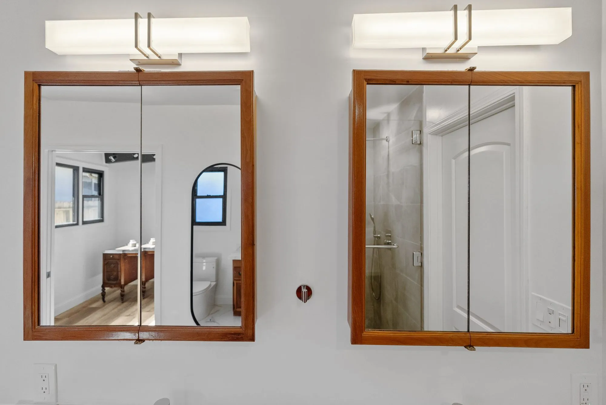Pair of wood-framed mirrored cabinets above a vanity with linear wall lights