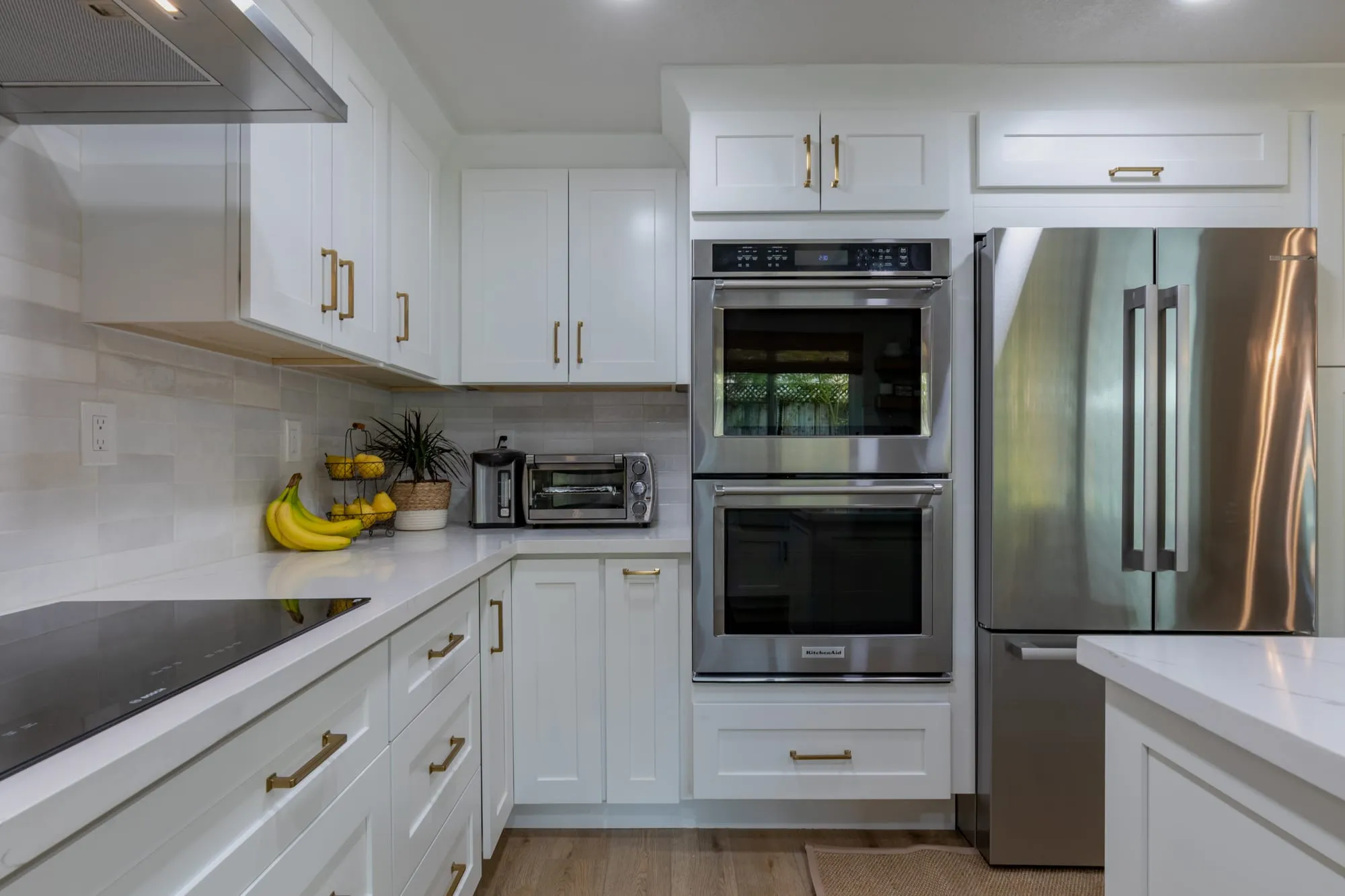 Stacked wall ovens beside the refrigerator in a white shaker tall run