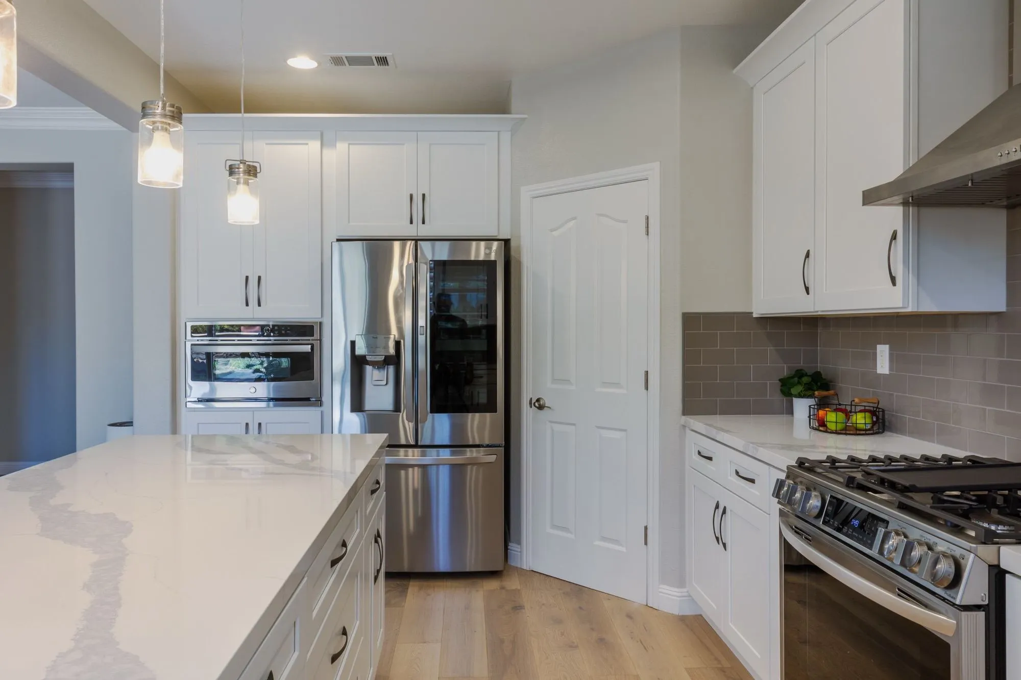 Stacked wall ovens and stainless refrigerator in white shaker cabinet run