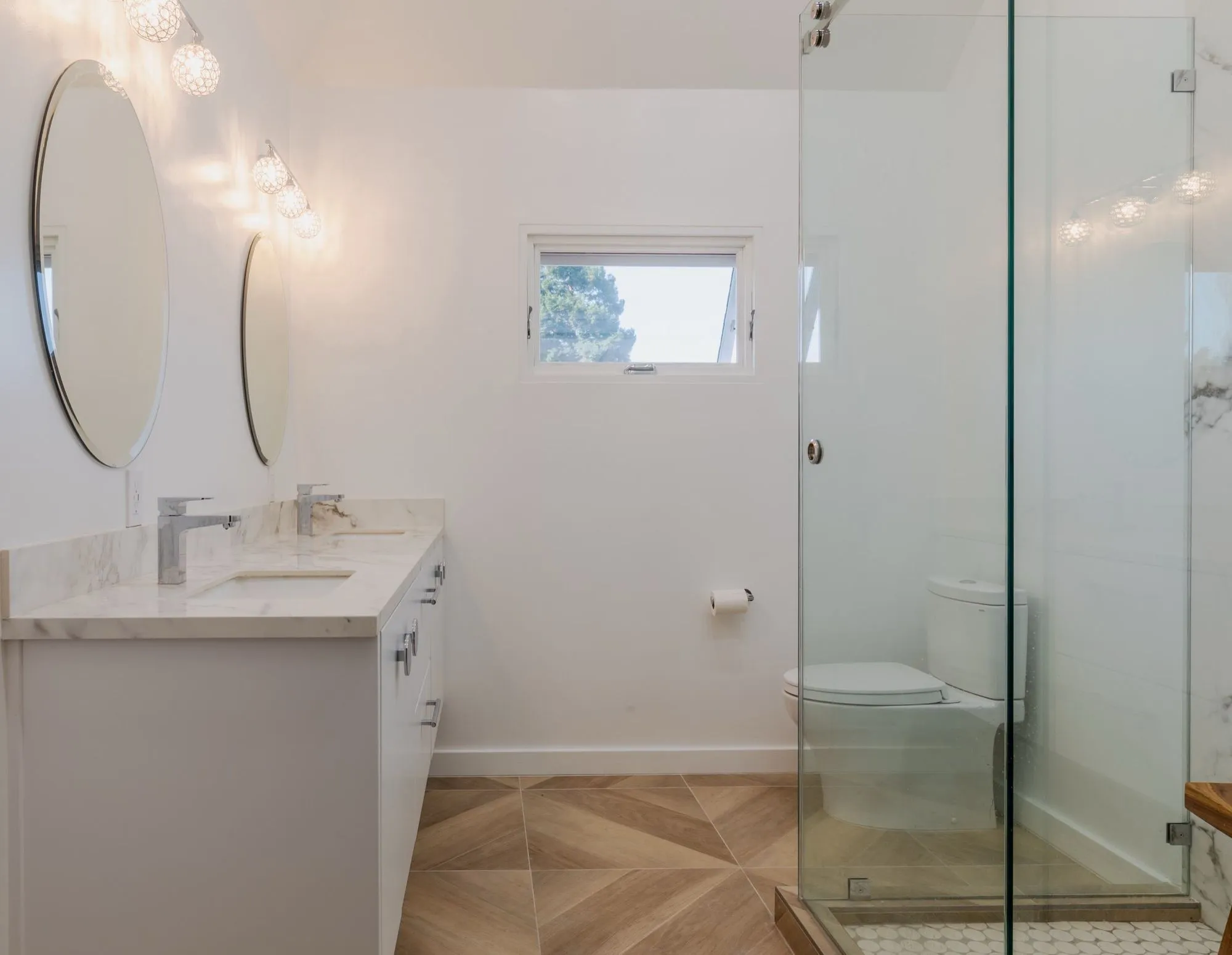 Bathroom after remodel, white vanity with stone counter and paired round mirrors